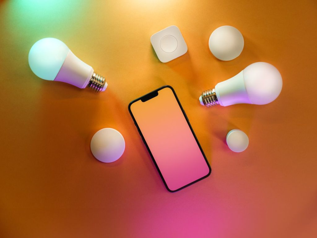 Top view of a smartphone with smart bulbs on a vibrant yellow background, depicting modern technology.