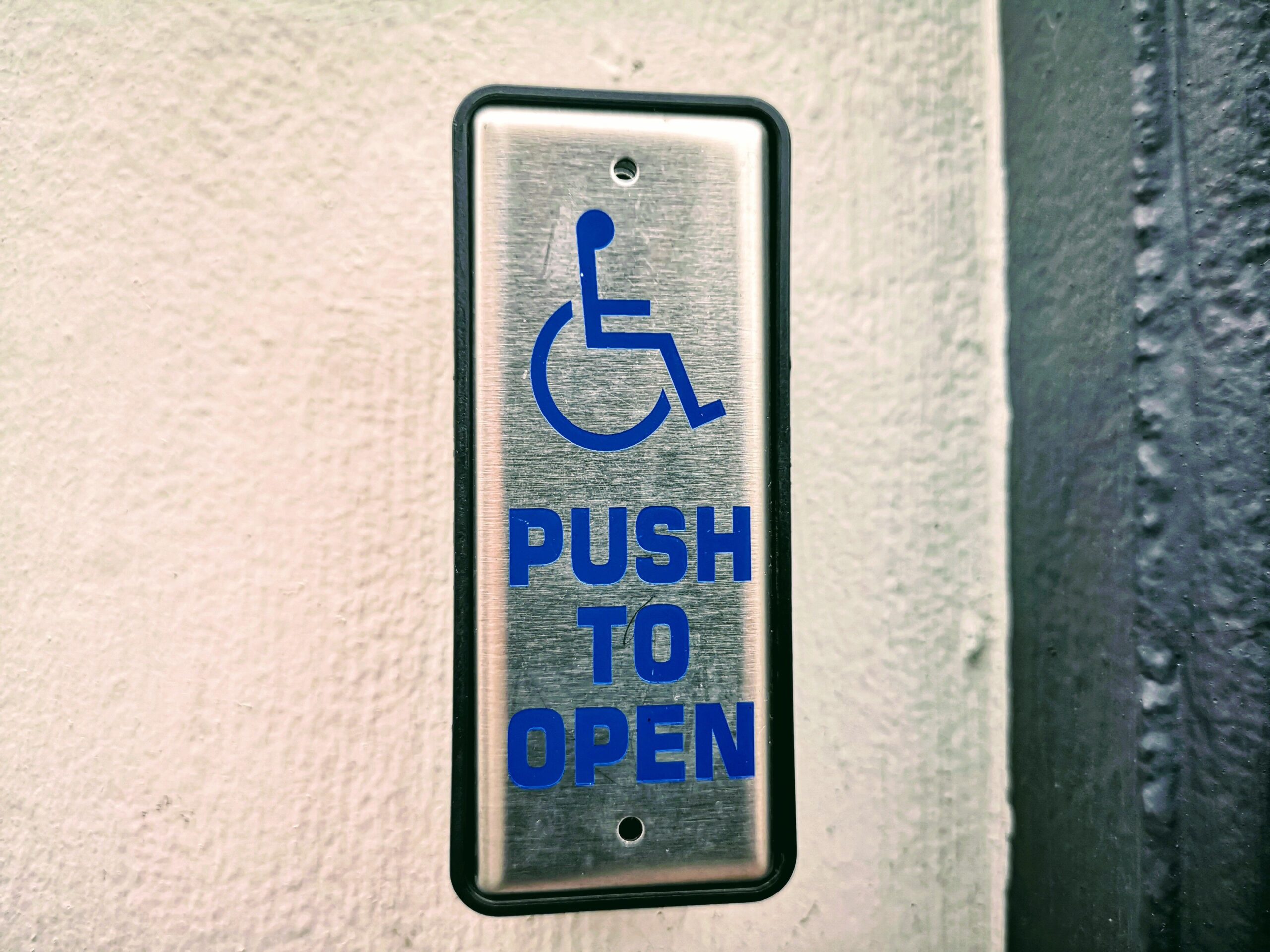 Close-up of a push button sign for accessibility on a white wall.